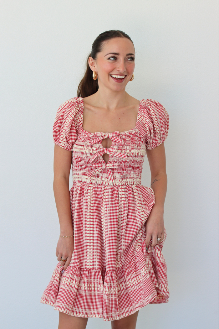 Woman wearing a red gingham mini dress with puff sleeves against a white background