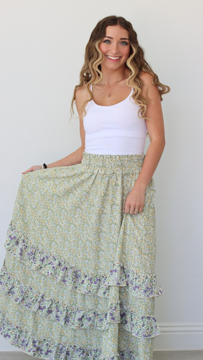 Woman wearing a white tank top and green floral skirt against a plain background