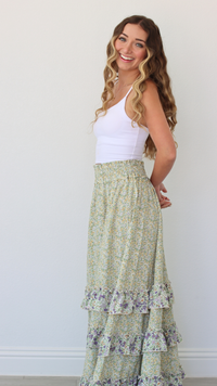Woman wearing a white tank top and green floral skirt against a plain background