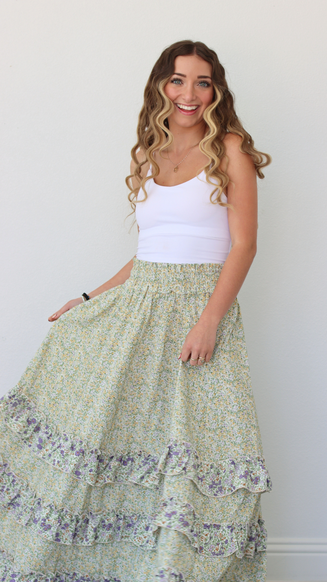 Woman wearing a white tank top and green floral skirt against a plain background