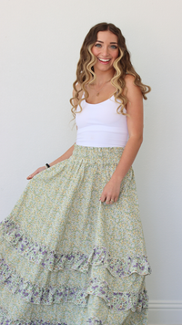 Woman wearing a white tank top and green floral skirt against a plain background