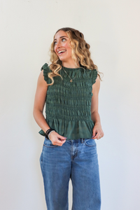 Woman wearing a green smocked top and blue jeans against a white background