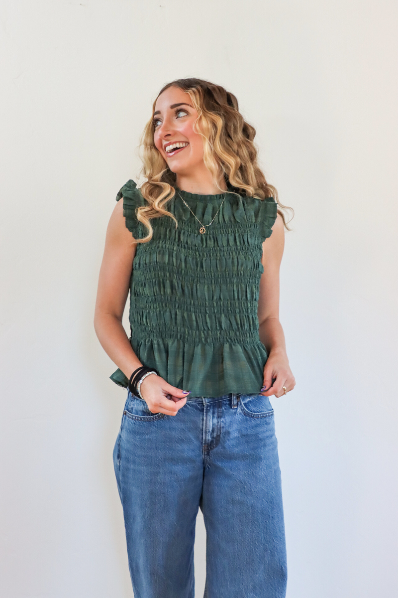 Woman wearing a green smocked top and blue jeans against a white background