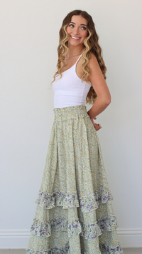 Woman wearing a white tank top and green floral skirt against a plain background