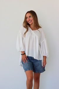 Woman wearing a white blouse and denim shorts against a plain background