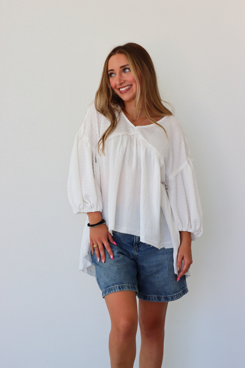 Woman wearing a white blouse and denim shorts against a plain background