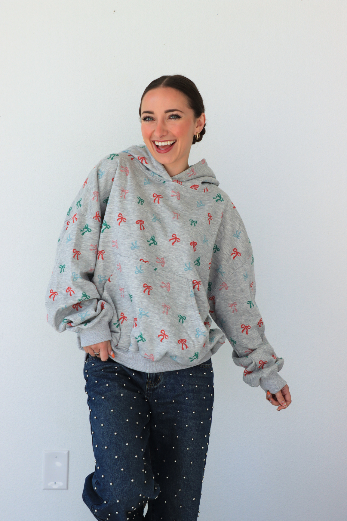 Woman wearing a gray hoodie with colorful patterns against a white wall