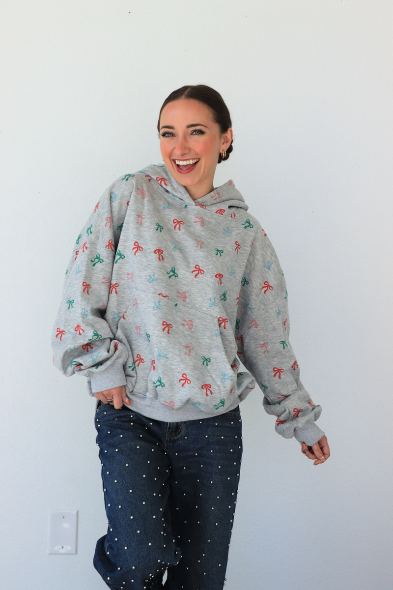 Woman wearing a gray hoodie with colorful patterns against a white wall