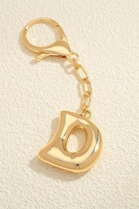 Gold keychain with letter 'd' on a beige background