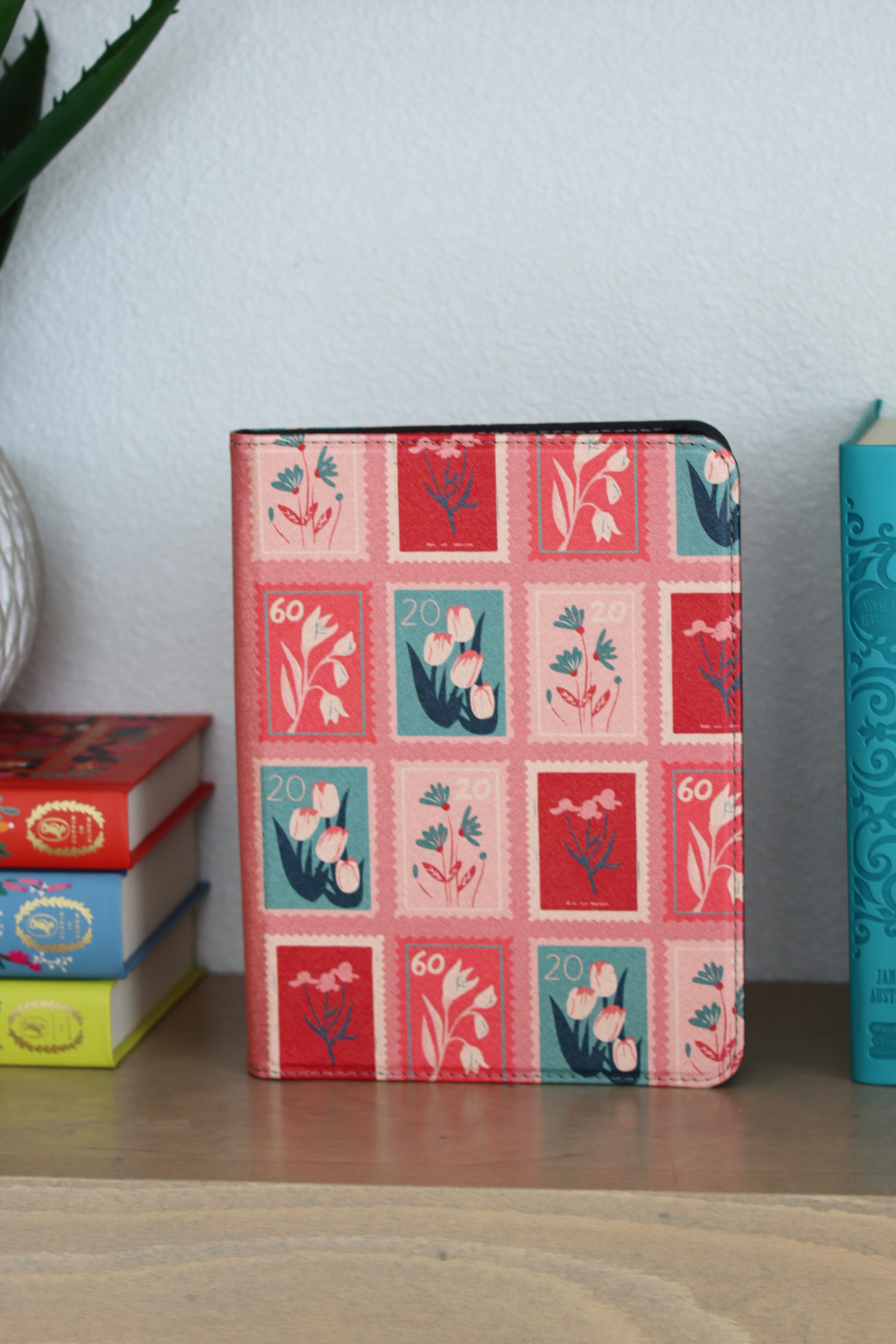 A nook case featuring a vintage-style postage stamp pattern with red, pink, and teal floral designs, photographed on a light fabric background.