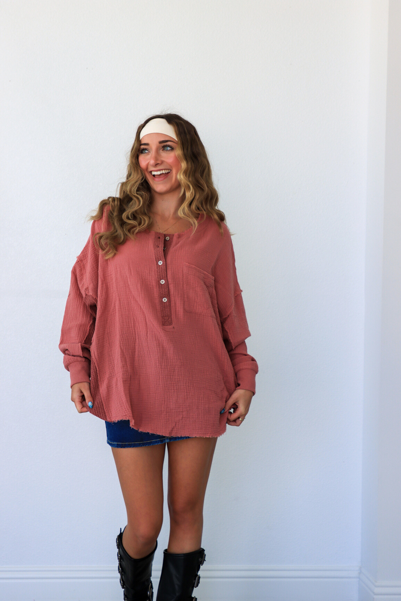 Woman wearing a pink long-sleeve shirt and black boots against a white wall