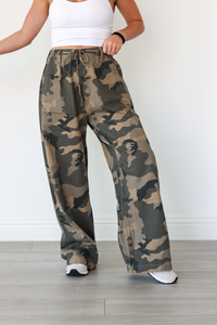 Camouflage pants worn by a person on a plain background