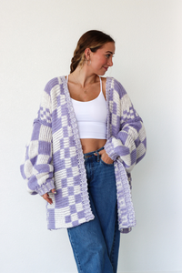 Woman wearing a purple and white checkered cardigan against a white background