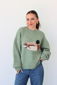 Woman wearing a green sweater with a duck design against a white background