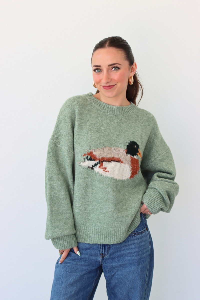 Woman wearing a green sweater with a duck design against a white background
