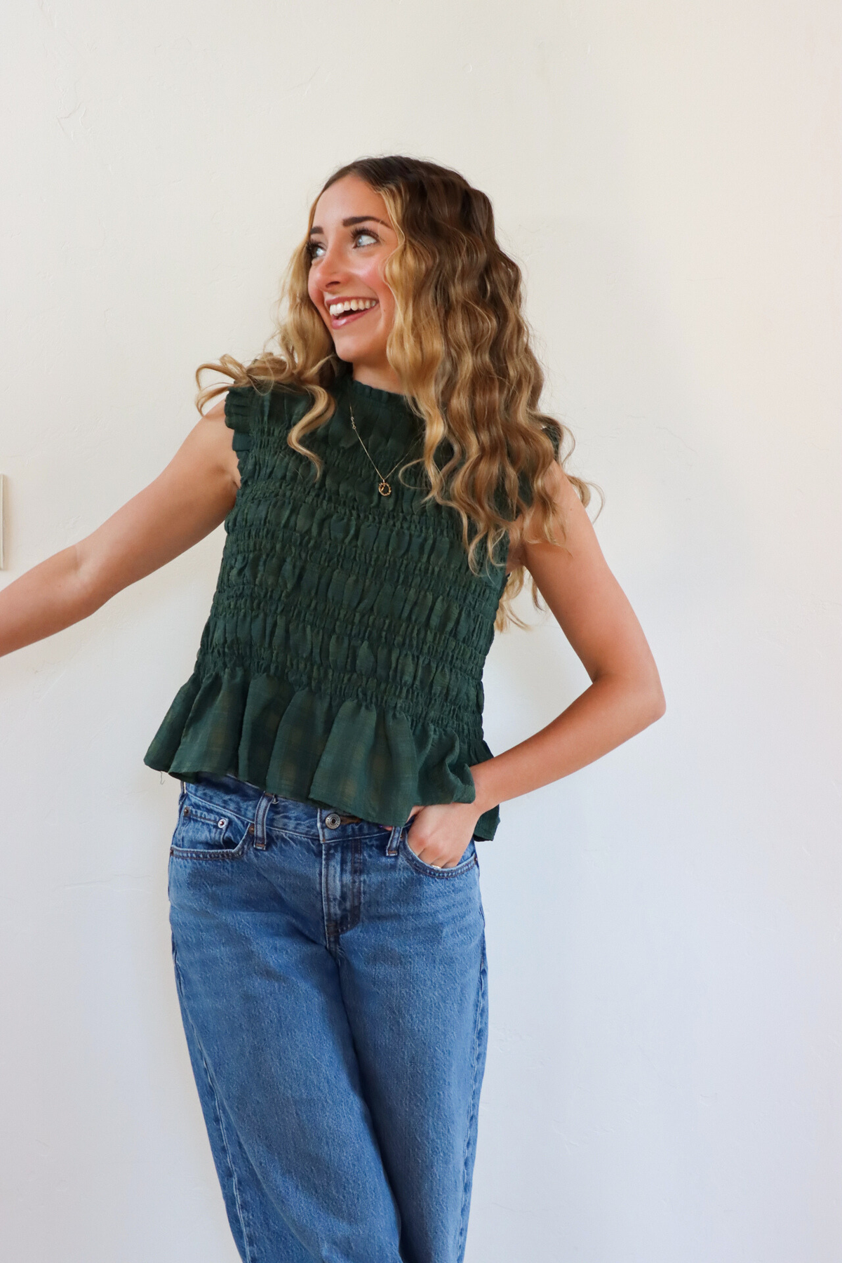 Woman wearing a green sleeveless top and blue jeans against a white background