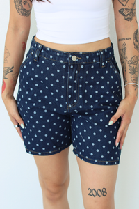 A person wearing dark blue denim shorts with a white polka dot pattern, paired with a white cropped tank top. The photo is cropped from the chest down against a plain white background.