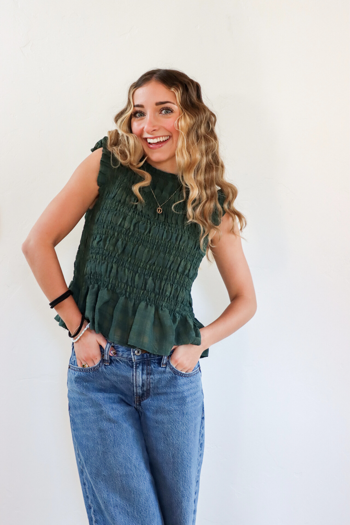 Woman wearing a green sleeveless top and blue jeans against a white background