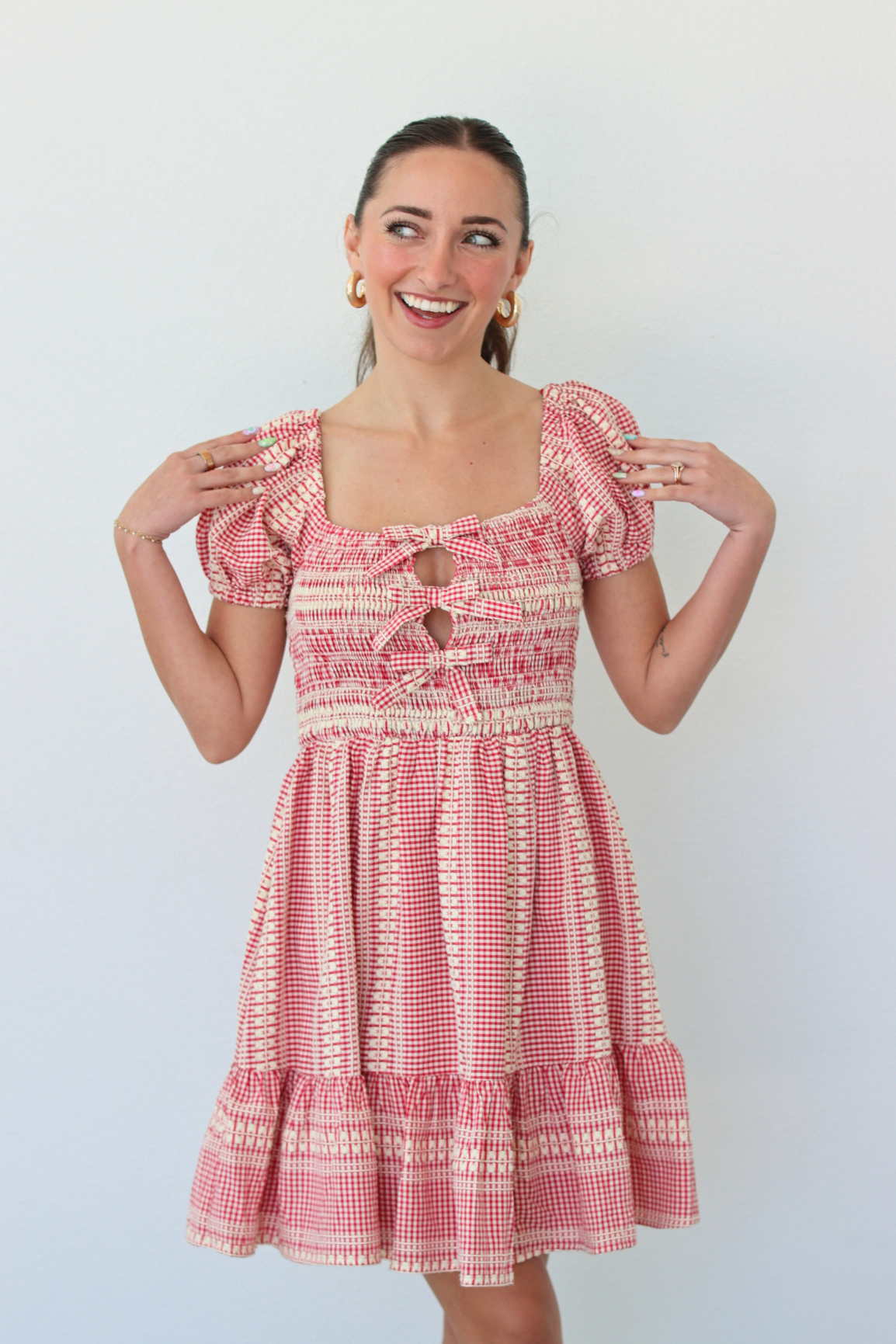 Woman wearing a red gingham mini dress with puff sleeves against a white background