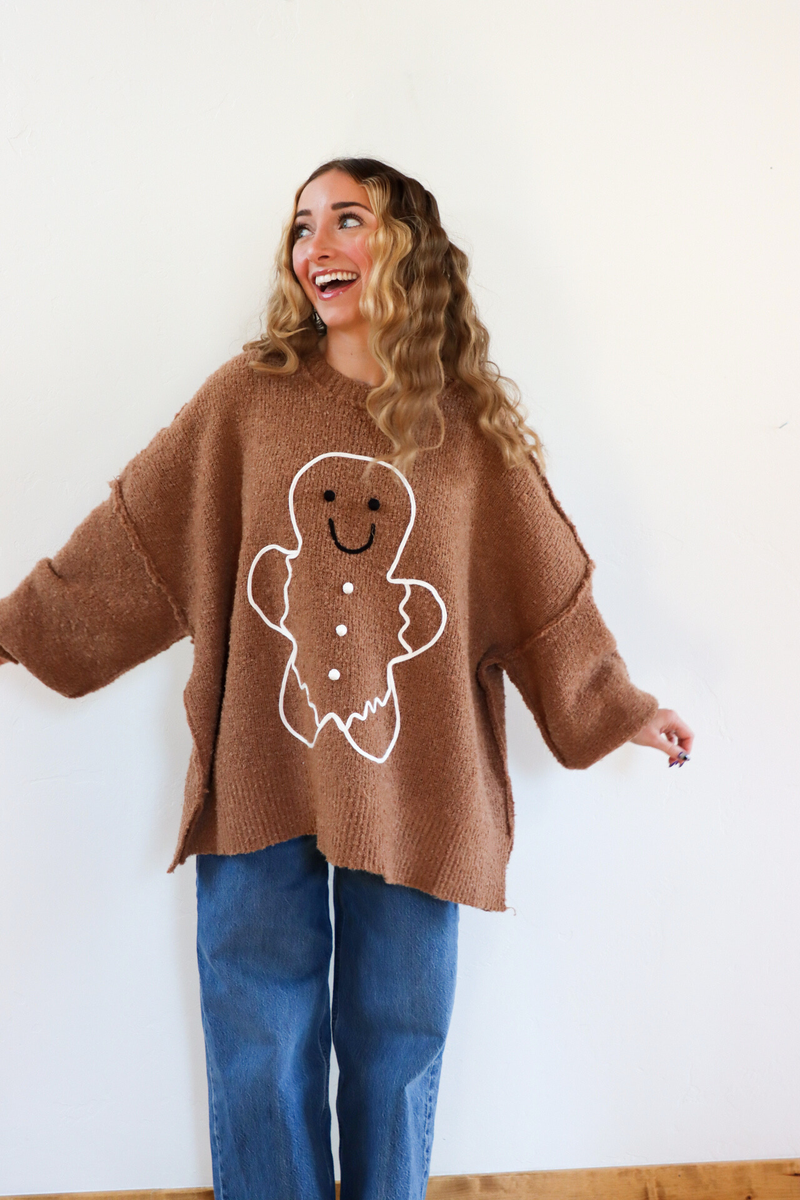 Woman wearing a brown sweater with a gingerbread man design against a white background