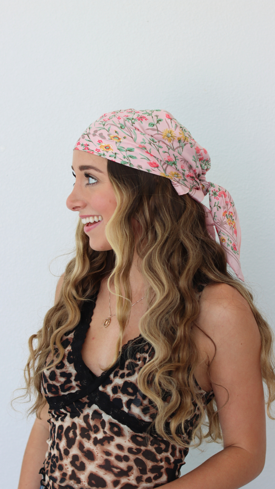 Woman wearing a floral headscarf and leopard print top on a white background