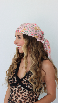 Woman wearing a floral headscarf and leopard print top on a white background