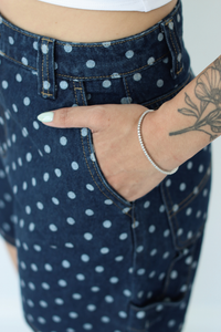 Close-up of a person wearing dark blue denim shorts with a white polka dot pattern, showing the front pocket and hand resting in the pocket.