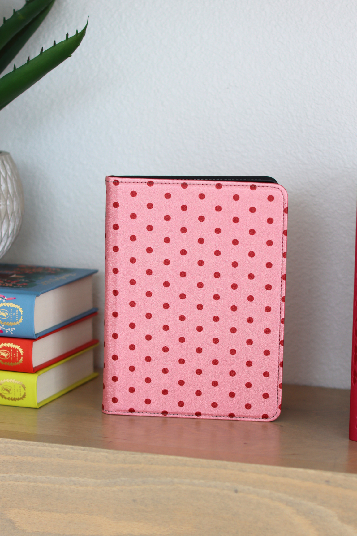 Pink polka dot kindle on a wooden shelf with books in the background