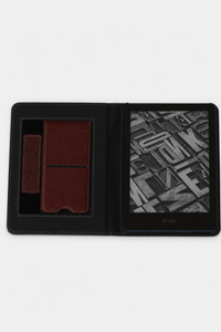 A dark red folio-style Kindle e-reader case shown open on a white background, with a kickstand and hand strap 