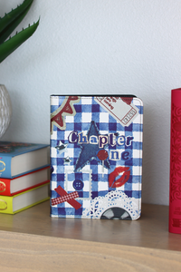 Kindle with a blue and white checkered cover on a shelf with books