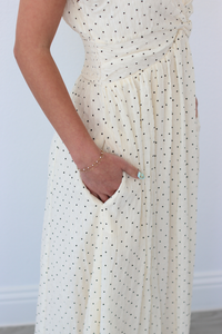 Woman wearing a white polka dot dress with pockets against a plain background