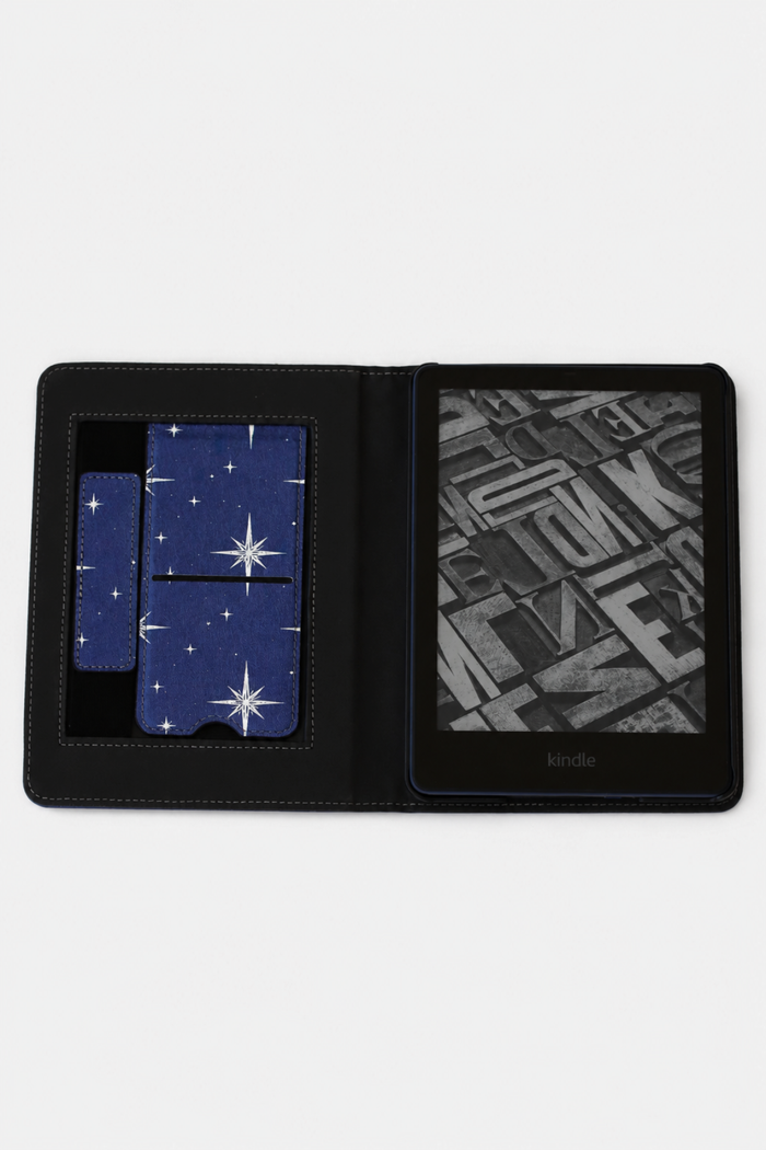 A black leather Kindle e-reader case shown open on a white background, featuring a blue starry night sky pattern on the card slots and a black-and-white book cover displayed on the screen.