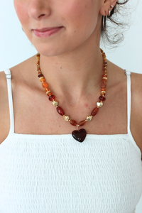 Woman wearing a beaded necklace with a heart pendant on a white background