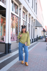 Woman wearing a v-neck green sweater with blue denim jeans