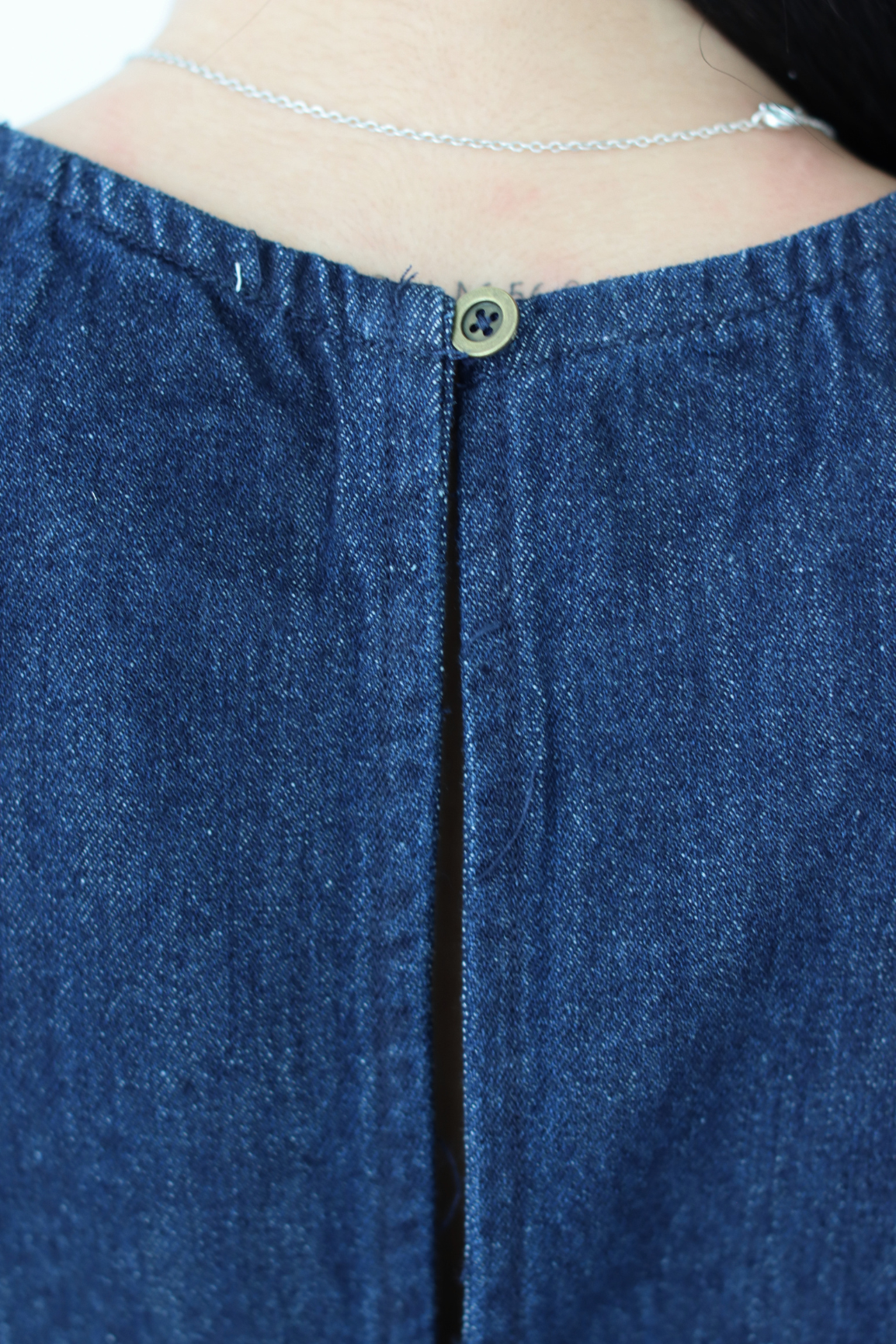 Close-up of a blue denim top with a button detail.
