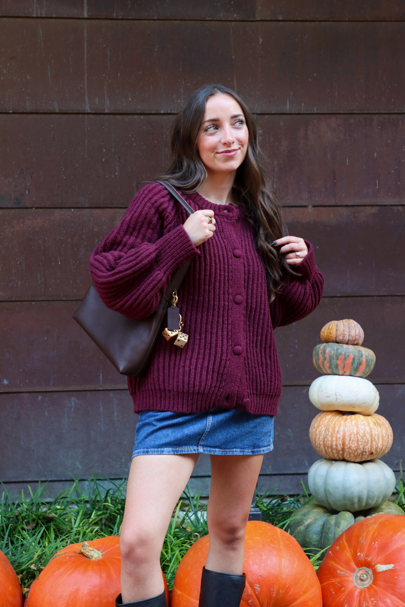 Woman in a purple sweater standing next to pumpkins against a wooden wall.