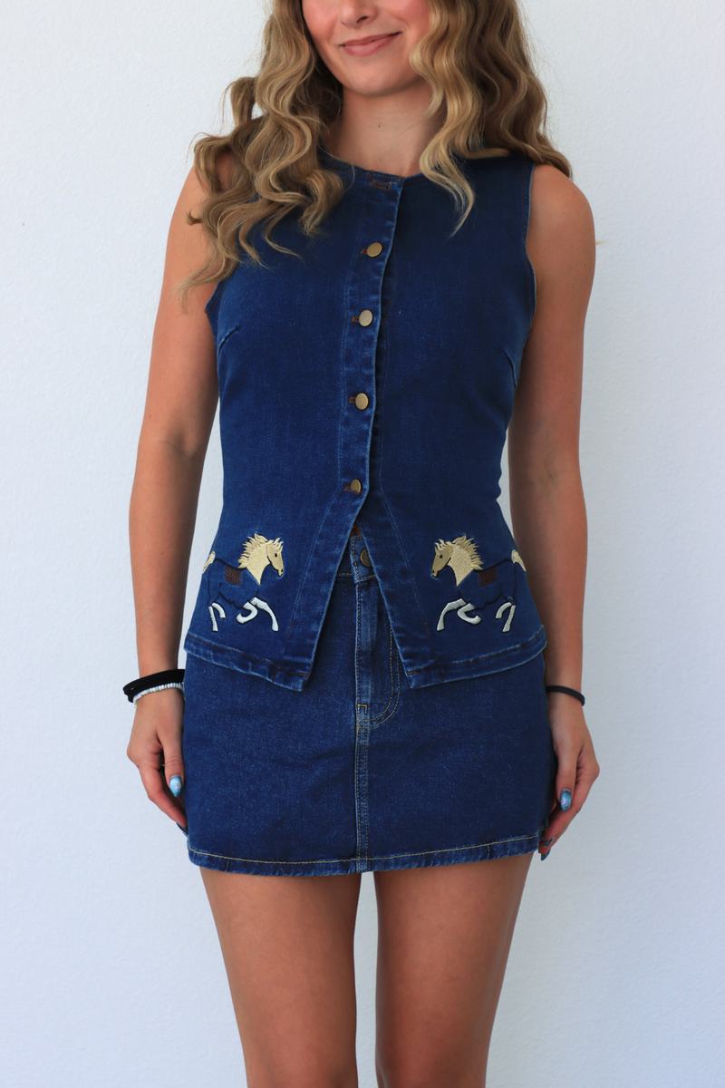 Woman wearing a blue denim dress with white embroidery against a white background