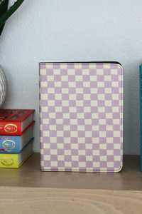 A nook case with a lavender and cream checkerboard pattern, standing upright on a wooden shelf next to books against a light blue wall.