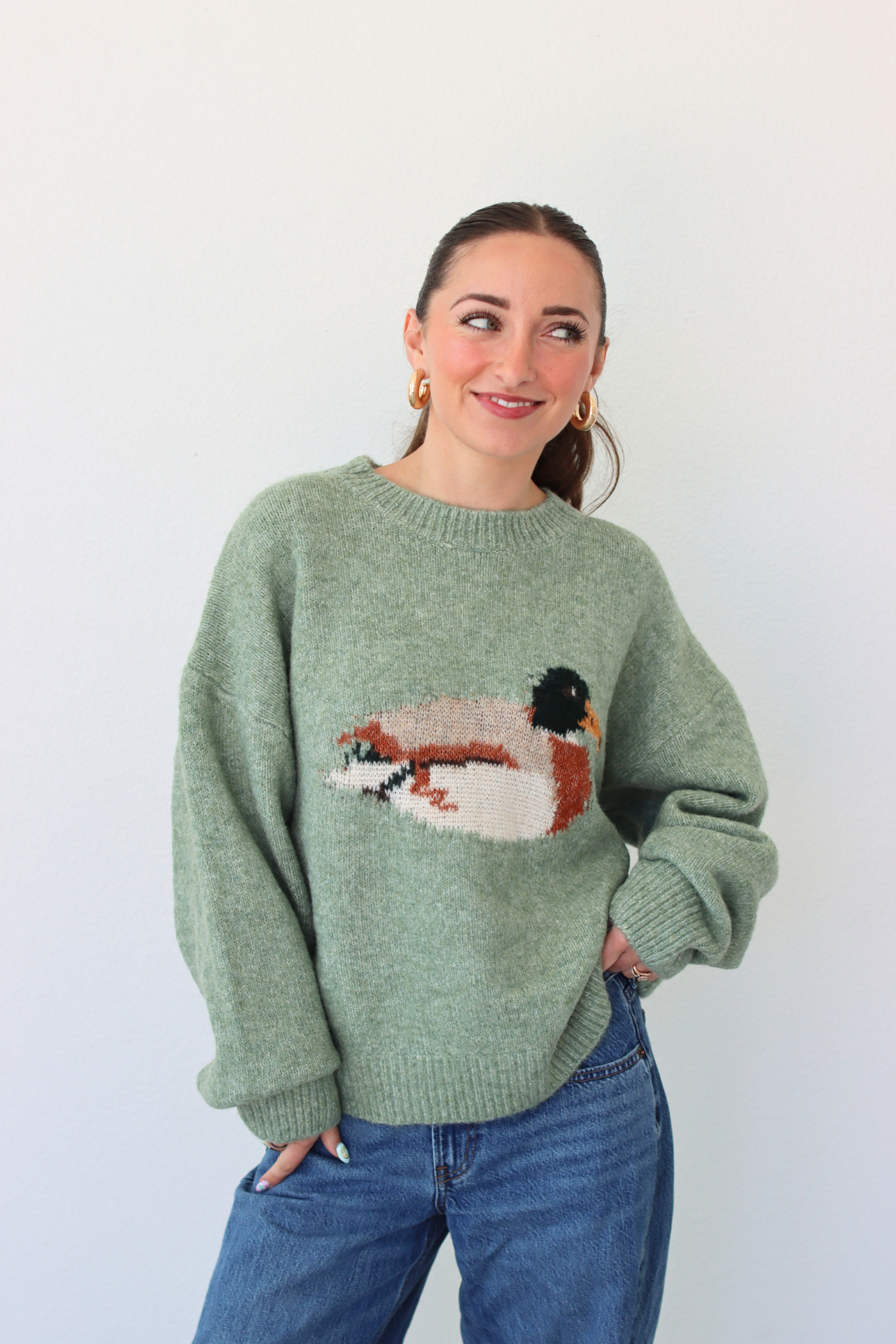 Woman wearing a green sweater with a duck design against a white background