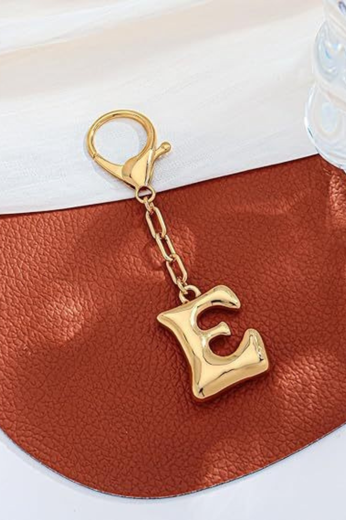 Gold keychain with letter 'E' on a brown leather surface