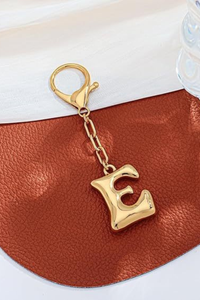 Gold keychain with letter 'E' on a brown leather surface