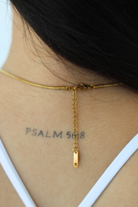 Close-up of the back of a person's neck wearing a delicate gold chain necklace with a small drop pendant. 