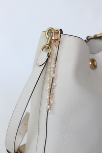 White handbag with gold hardware and a decorative chain on a light gray background