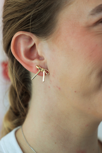 Close-up of a person wearing a gold earring with three small bars.