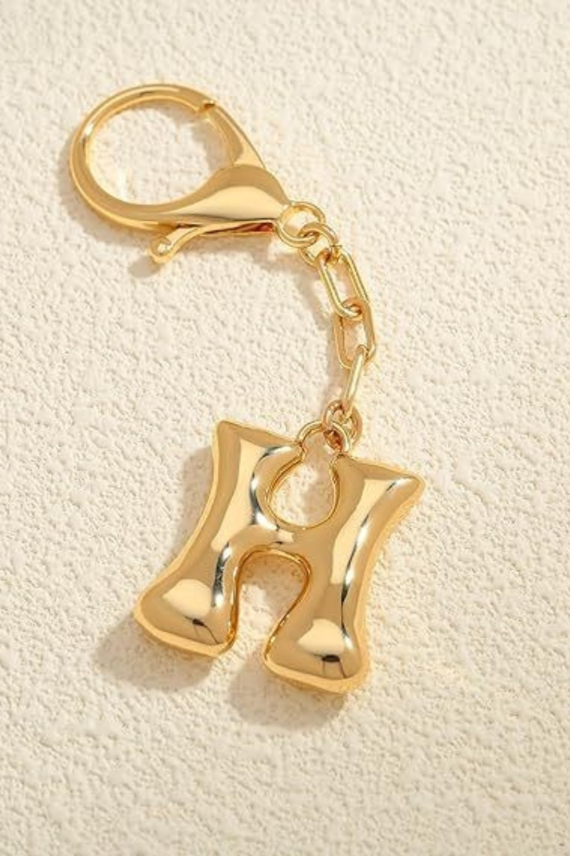 Gold keychain with letter 'H' on a beige textured background