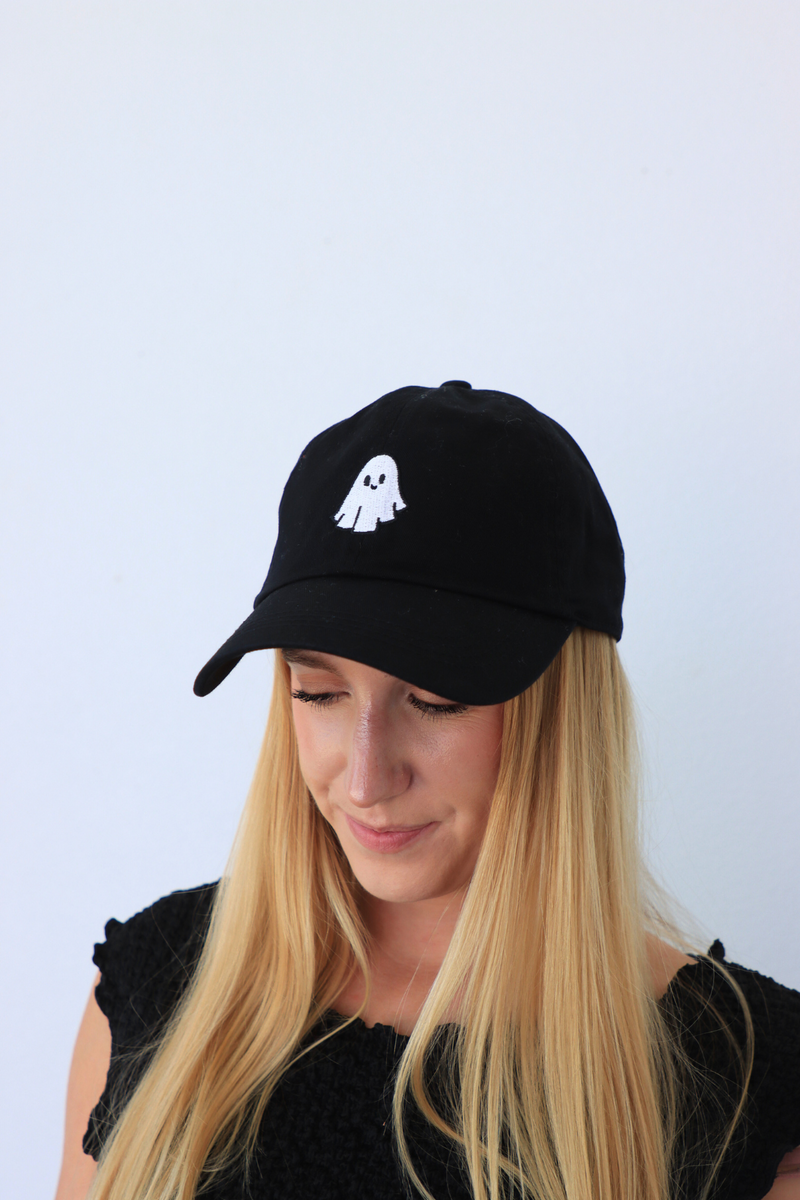 Person wearing a black cap with a white ghost design on a light blue background