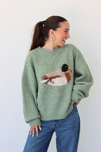 Woman wearing a green sweater with a duck design against a white background