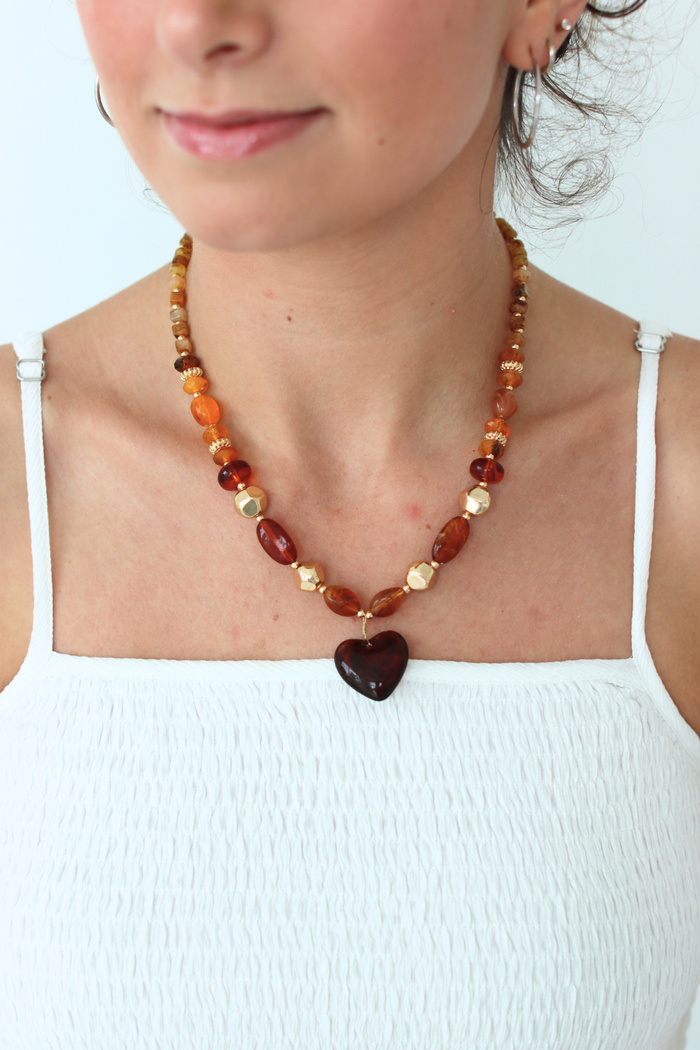 Person wearing a necklace with a heart-shaped pendant on a white background