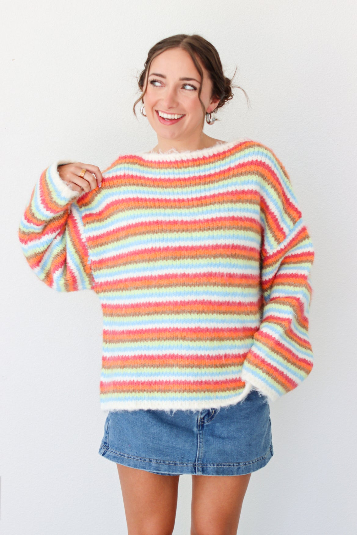 Woman wearing a multi color striped sweater with a denim mini skirt 