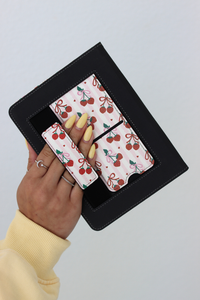 Hand holding a kindle case with cherry-patterned items inside on a light gray background